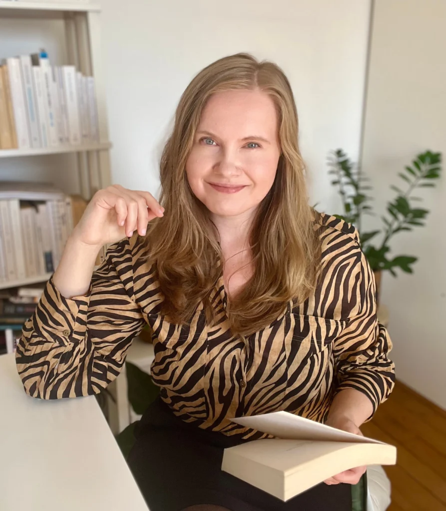 Portrait of dr. Ewelina Chwiejda, founder of Art Wanderer, sitting at the desk with a book