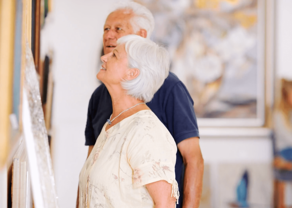 Older couple viewing an artwork in a gallery, illustrating the wellbeing benefits of mindful art experiences.